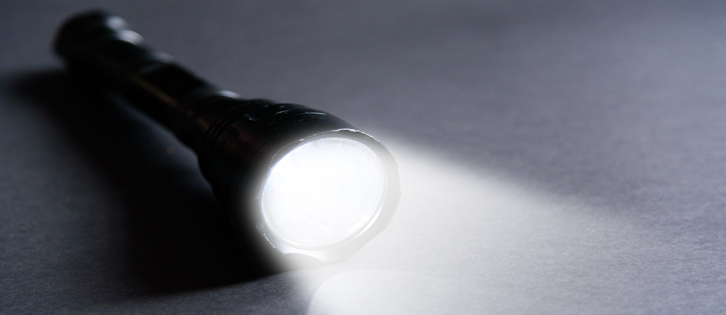 Picture of a flashlight beaming a light on the floor in a dark room.