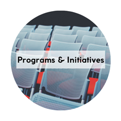 Circular icon with the words "Programs & Initiatives" written across the center. Background is image of rows of chairs.